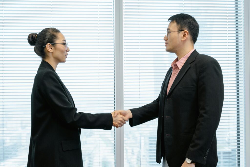 Two business professionals shaking hands in a modern office setting, symbolizing partnership.